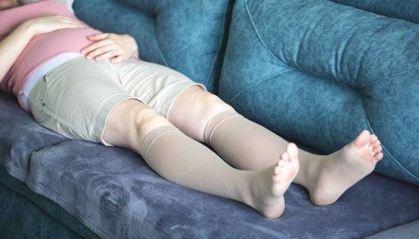 Woman resting on sofa, wearing beige medical compression socks for women for support.