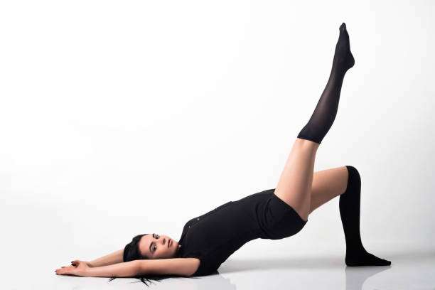 Flexible woman in black leotard and compression socks for women stretching.