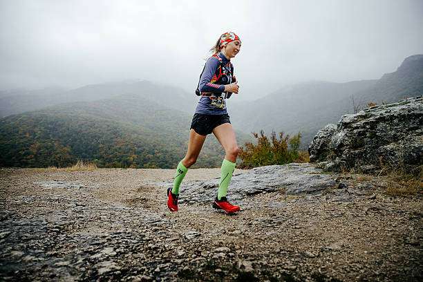 Woman trail running in green compression socks for women through misty mountains.