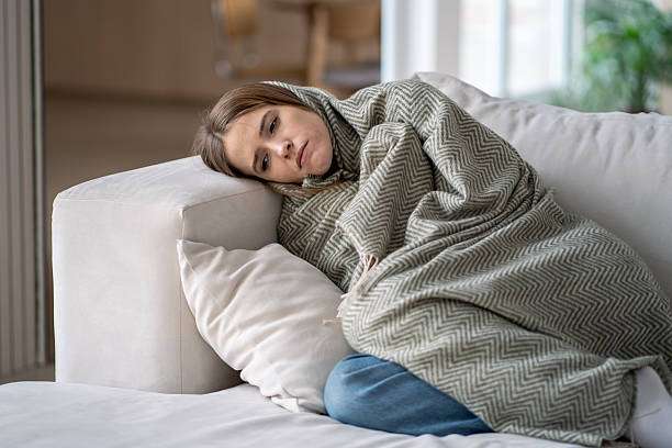 Woman curled up on couch, feeling sick. Compression socks for women offer soothing support.